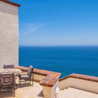 A private terrace overlooks the expansive blue ocean, with comfortable seating for sipping morning coffee or watching sunset unfold. The elevated, open-air setting frames endless coastal views.