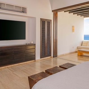 Wake up to stunning ocean views through your bedroom's open terrace, where bright blue waters meet the horizon and gentle breezes drift in through exposed-beam ceilings.
