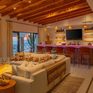 Sink into this plush sectional while admiring ocean views through floor-to-ceiling windows. The warm wood beams and vibrant bar create a perfect gathering space.