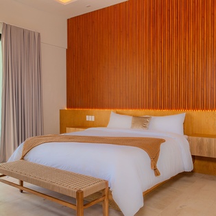 Sink into crisp white linens and warm wood textures in your serene bedroom, where floor-to-ceiling windows frame tropical views from your private balcony.