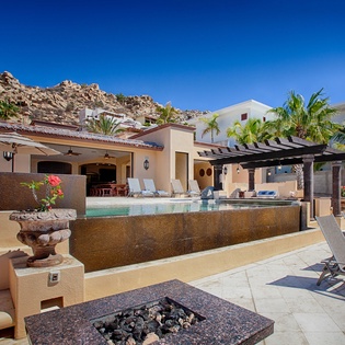 Hillside property featuring a swimming pool, covered pergola, and sunbathing area set against dramatic desert rock formations under clear blue skies.