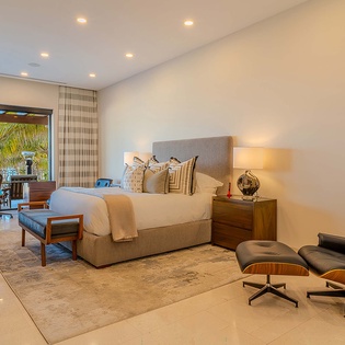 Unwind in your serene bedroom, where plush bedding and a designer lounge chair invite you to relax. Step through the glass doors to your private balcony overlooking swaying palms and the ocean beyond.