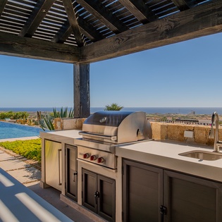 Your outdoor kitchen awaits with premium grill and prep space under a shaded pergola, overlooking the sparkling pool and breathtaking ocean views.