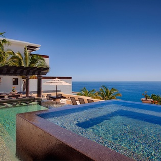 Modern luxury property featuring multi-level infinity pools with stunning ocean views, surrounded by lush palms and contemporary pergola architecture along the coastline.