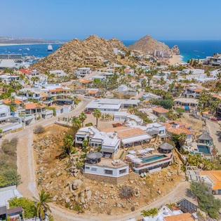 Stunning aerial view of a coastal hillside community with luxury homes, dramatic rock formations, and pristine blue waters stretching to the horizon.