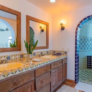 Step into this vibrant bathroom where handcrafted tilework meets warm wood accents. The arched shower awaits, framed by stunning blue mosaics that turn your daily routine into a colorful escape.