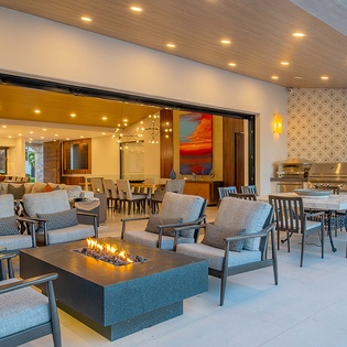 Relax in this covered patio with comfortable seating and a modern fire feature, seamlessly connecting indoor and outdoor dining areas perfect for unwinding after your day.