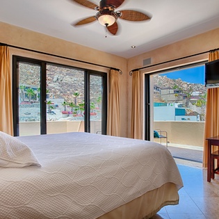 Wake up to mountain and poolside views from your serene bedroom, where golden drapes frame expansive windows and a tropical ceiling fan keeps you cool throughout your stay.
