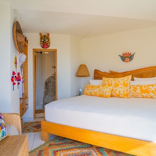 Your colorful bedroom blends Mexican charm with modern comfort—crisp white linens, vibrant orange pillows, and authentic artwork create your perfect retreat.