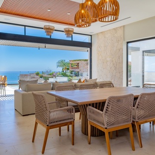 Gather around this stunning dining table where warm wood meets ocean views, creating the perfect setting for memorable meals together.