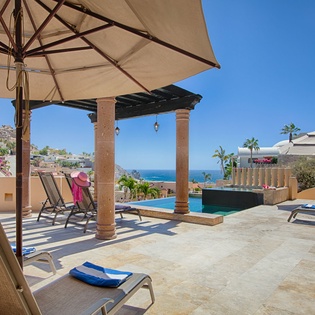 A sun-drenched pool terrace offers loungers under umbrellas and a covered pergola, with sparkling ocean views framing your private hillside retreat.
