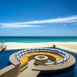 Stunning beachfront pool with sunken fire pit seating area overlooking pristine white sand and turquoise waters.