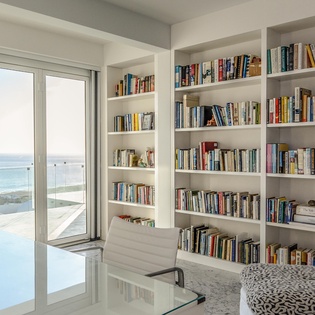 Your private library with floor-to-ceiling books and stunning sea views creates the perfect reading retreat.