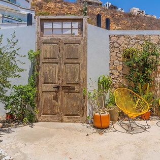 Bright yellow seating invites you to relax in this charming stone-walled courtyard with rustic wooden doors and lush greenery dappling sunlight overhead.