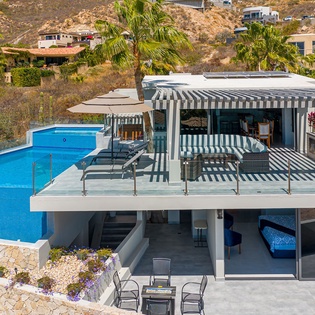 Modern hillside villa featuring infinity pool and covered outdoor dining area with mountain backdrop.