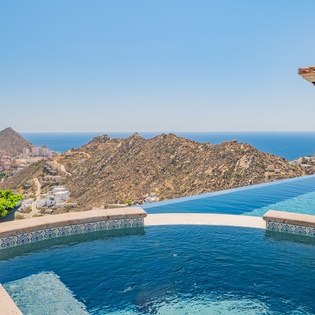 Stunning infinity pool with panoramic ocean views and desert mountain backdrop creates the perfect luxury escape.
