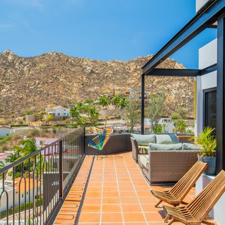 Spacious terrace overlooking a charming neighborhood with scenic mountain backdrop. Furnished with outdoor seating and lounge chairs for relaxing under the sun.