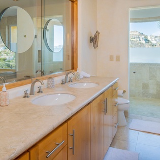 Luxurious dual-sink vanity with marble countertops and stunning hillside views through floor-to-ceiling windows.