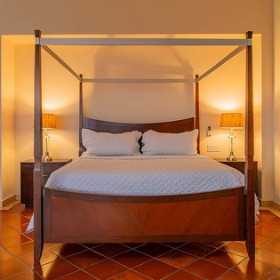Unwind in this elegant bedroom featuring a handcrafted four-poster bed, warm terracotta tile floors, and soft ambient lighting that creates a peaceful retreat for your stay.