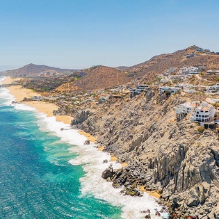 Aerial view of the rugged coastline featuring turquoise waters, sandy beaches, and hillside properties in the surrounding neighborhood—a stunning location near your getaway.
