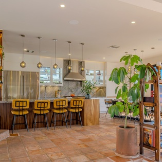 Gather around the sleek kitchen island with stylish pendant lighting, where modern design meets natural warmth through wood tones and lush greenery throughout the space.