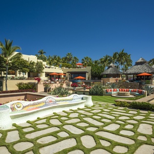 A stunning tropical resort property featuring beautiful landscaping with palm trees and traditional thatched-roof buildings under bright blue skies.
