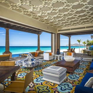 Your stunning beachfront living room opens to endless turquoise waters, where vibrant décor meets ocean breezes through soaring arches.
