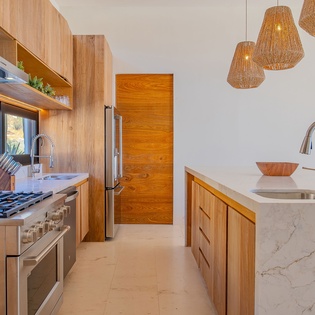 Your gourmet kitchen awaits with warm wood cabinetry, marble counters, and woven pendant lights creating the perfect culinary retreat.