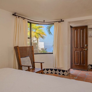 Unwind in your peaceful bedroom with charming tilework and a cozy reading nook, where palm-framed windows reveal stunning ocean views just beyond your doorstep.