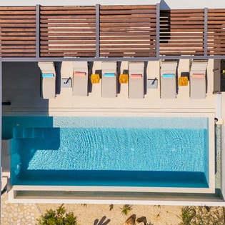 Aerial view of a pristine swimming pool surrounded by modern decking and privacy screening at this vacation property.