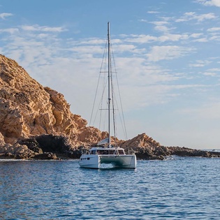 A catamaran anchors in crystal-clear waters beside dramatic coastal cliffs, perfect for exploring hidden coves and serene sailing adventures in the surrounding area.