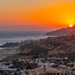 Stunning coastal sunset view over beachfront properties and dramatic hillside landscape.