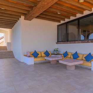 Settle into your private covered terrace, where warm wood beams shelter vibrant built-in seating. Soft cushions and bold blue pillows invite you to unwind in style under the open sky.