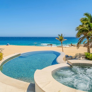 Beachfront property featuring a private swimming pool and hot tub overlooking pristine golden sands and turquoise ocean waters, framed by swaying palms.