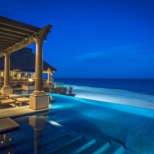 Stunning infinity pool meets ocean horizon beneath dramatic evening sky, with elegant terrace seating creating perfect beachfront ambiance.