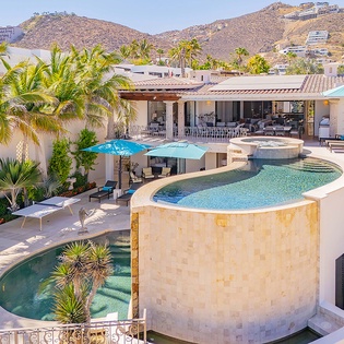 A luxurious desert retreat nestled in the hillside, featuring tiered pools, lush tropical gardens, and expansive terraces with dramatic mountain and residential views.