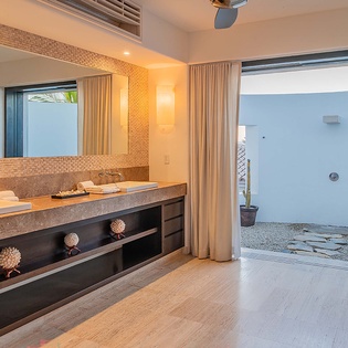 Step into your private spa-like bathroom where natural textures blend seamlessly with modern luxury. Fresh towels await, and your open-air shower promises a tranquil escape under the palms.
