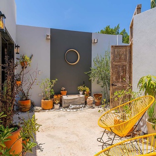 Colorful courtyard with terracotta pots and bright yellow seating surrounded by lush greenery—your peaceful outdoor retreat.
