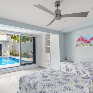 Wake up to your private pool view through floor-to-ceiling windows in this serene bedroom with twin beds and refreshing ceiling fan.
