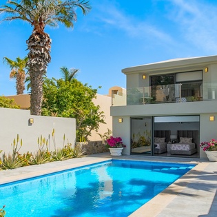 Modern villa with private pool surrounded by tropical palms and desert landscaping under sunny skies.