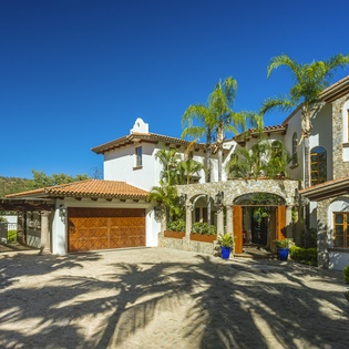 Stunning Mediterranean-style villa with stone accents and tropical landscaping under brilliant blue skies.