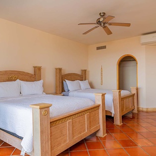 Sink into crisp, white linens on these handcrafted wooden beds, where warm terracotta tiles and a gentle ceiling fan promise restful nights in your spacious retreat.