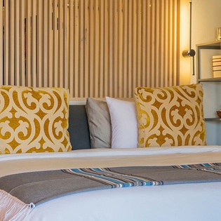 Sink into crisp white linens and vibrant gold-patterned pillows—your cozy retreat awaits with modern shelving and warm lighting to make you feel instantly at home.
