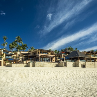 Beachfront resort buildings with palm trees line the pristine sandy shore, offering a tropical vacation setting with stunning ocean access.