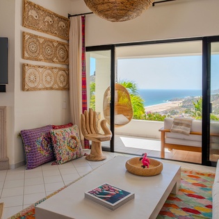Relax in your vibrant living room where colorful textiles meet stunning ocean views through floor-to-ceiling windows.