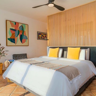 Drift off in your thoughtfully designed bedroom, where vibrant artwork and soft linens welcome you to a restful retreat beneath the gentle hum of a ceiling fan.