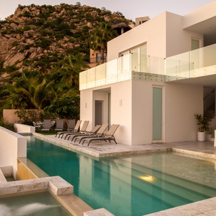 Modern villa nestled against dramatic rocky hillside with pristine pool and contemporary architecture at golden hour.