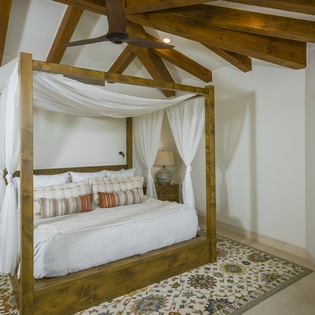 Drift off in your romantic four-poster bed beneath rustic wooden beams, where flowing white curtains create your private sanctuary.