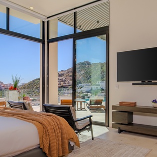 Wake up to stunning mountain views through floor-to-ceiling windows in your modern bedroom with balcony access and entertainment setup.