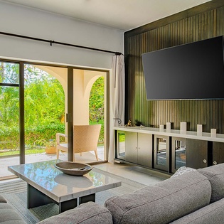 Unwind in your spacious living room with plush seating and natural light pouring through sliding doors that open to lush garden greenery—your perfect spot to relax after a day of exploring.